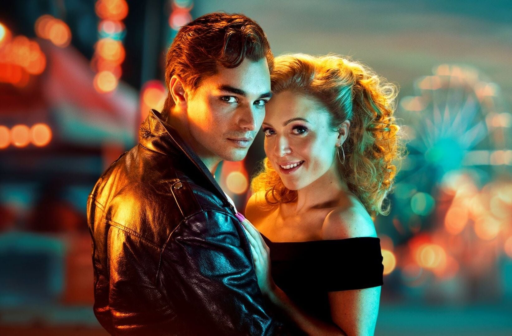 Två huvudkaraktärer från Grease poserar tillsammans framför färgglada nöjesljus inför föreställning på Rondo